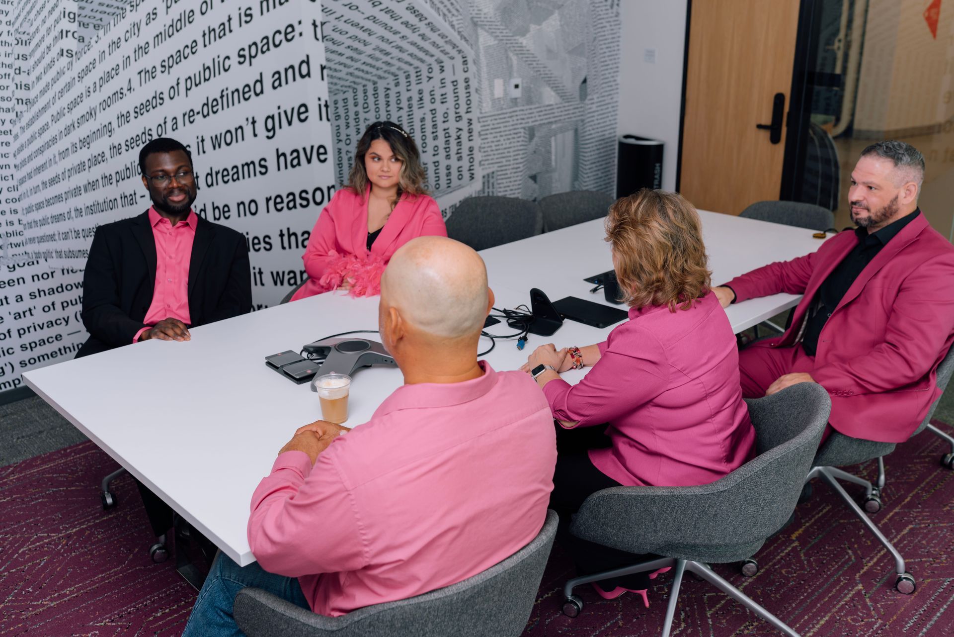 A group of people in pink suits are sitting around a table.