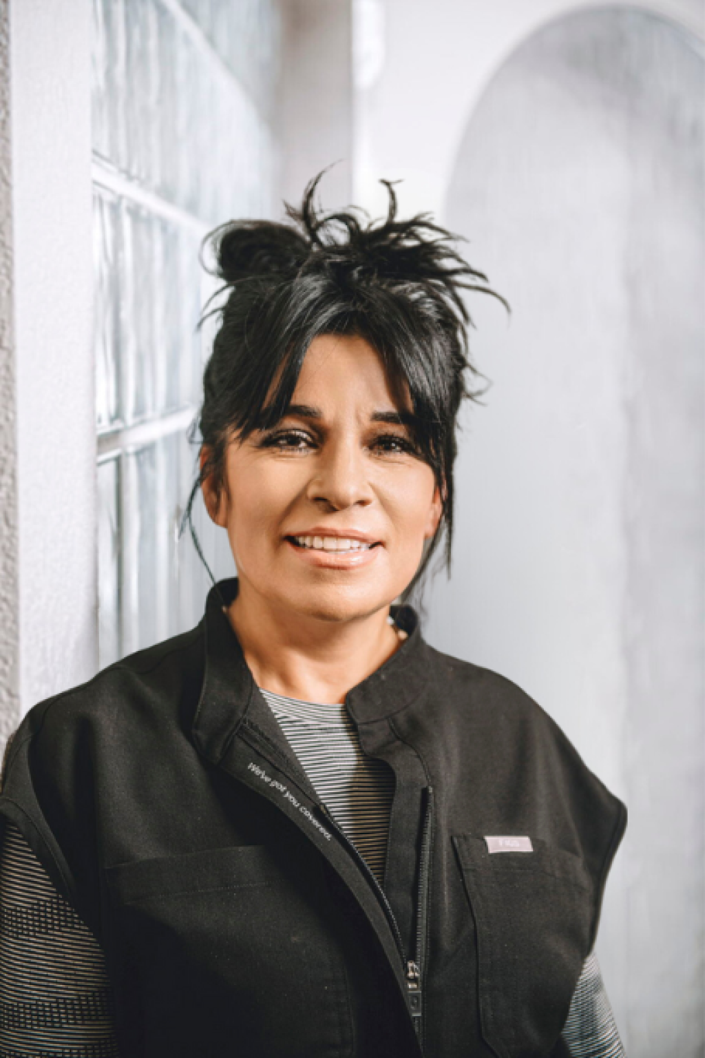 The woman is wearing a black vest and smiling for the camera.