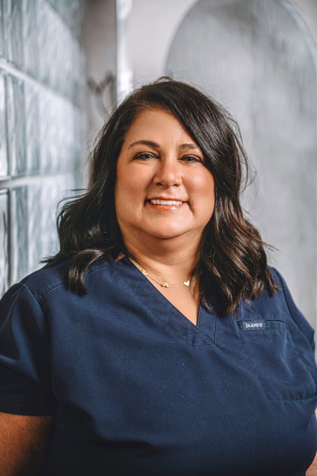 A woman in a blue scrub top is smiling for the camera.