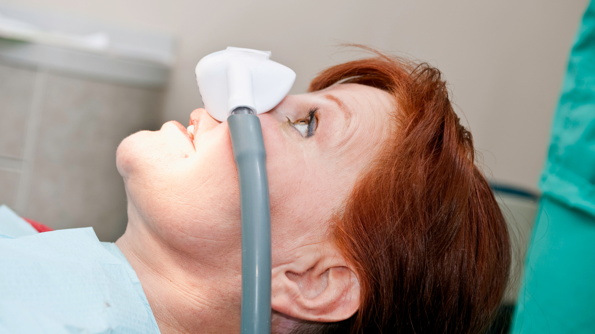 A woman is laying in a dental chair with an oxygen mask on her face.