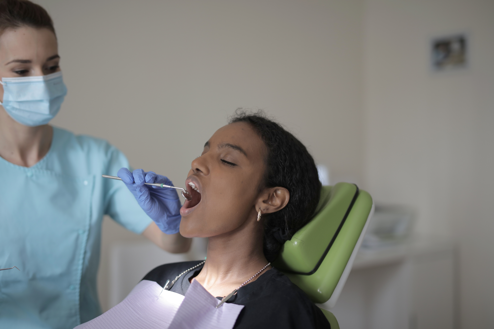 Dentist in blue gloves examining a patient in a dental chair with mouth open