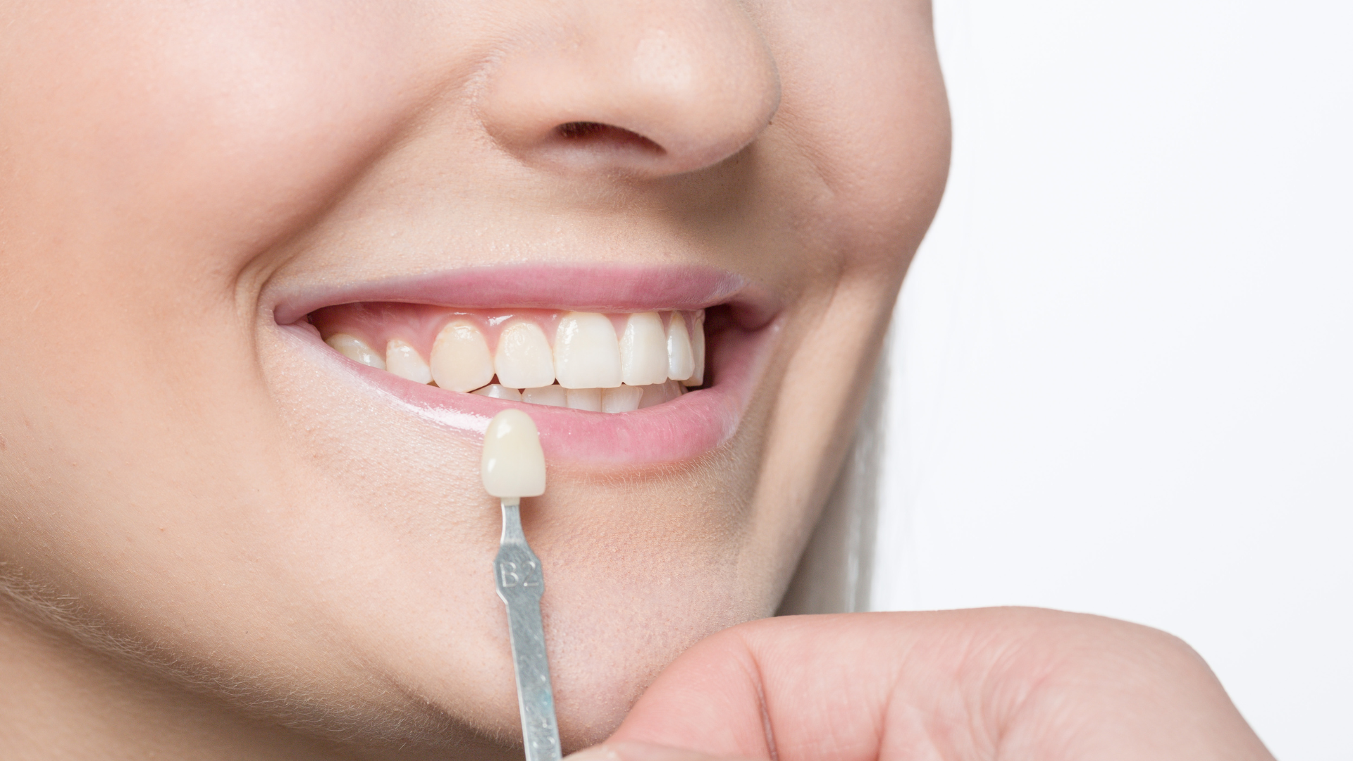 A woman is holding a tooth shade in front of her teeth.