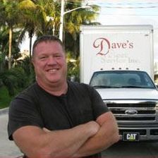 A man is standing in front of a truck with his arms crossed.