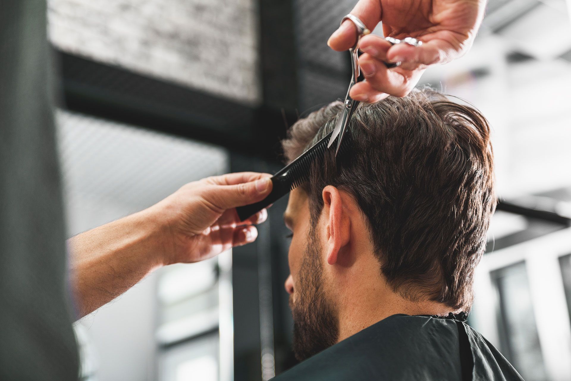 A barber uses scissors to trim the hair of a person seated in a salon chair.