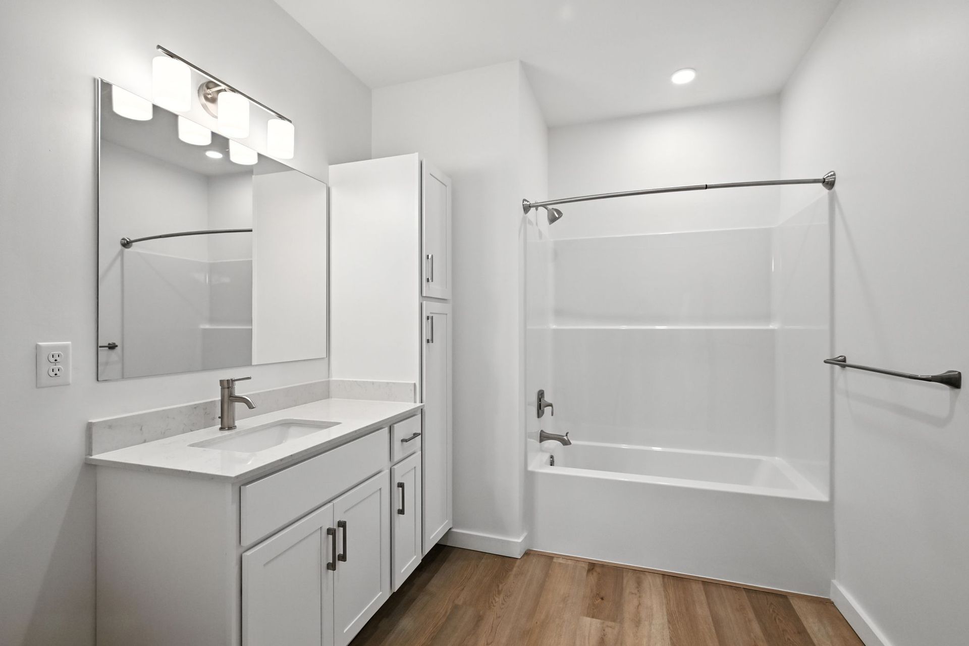 White bathroom with vanity, storage cabinet, bathtub, and light wood flooring.