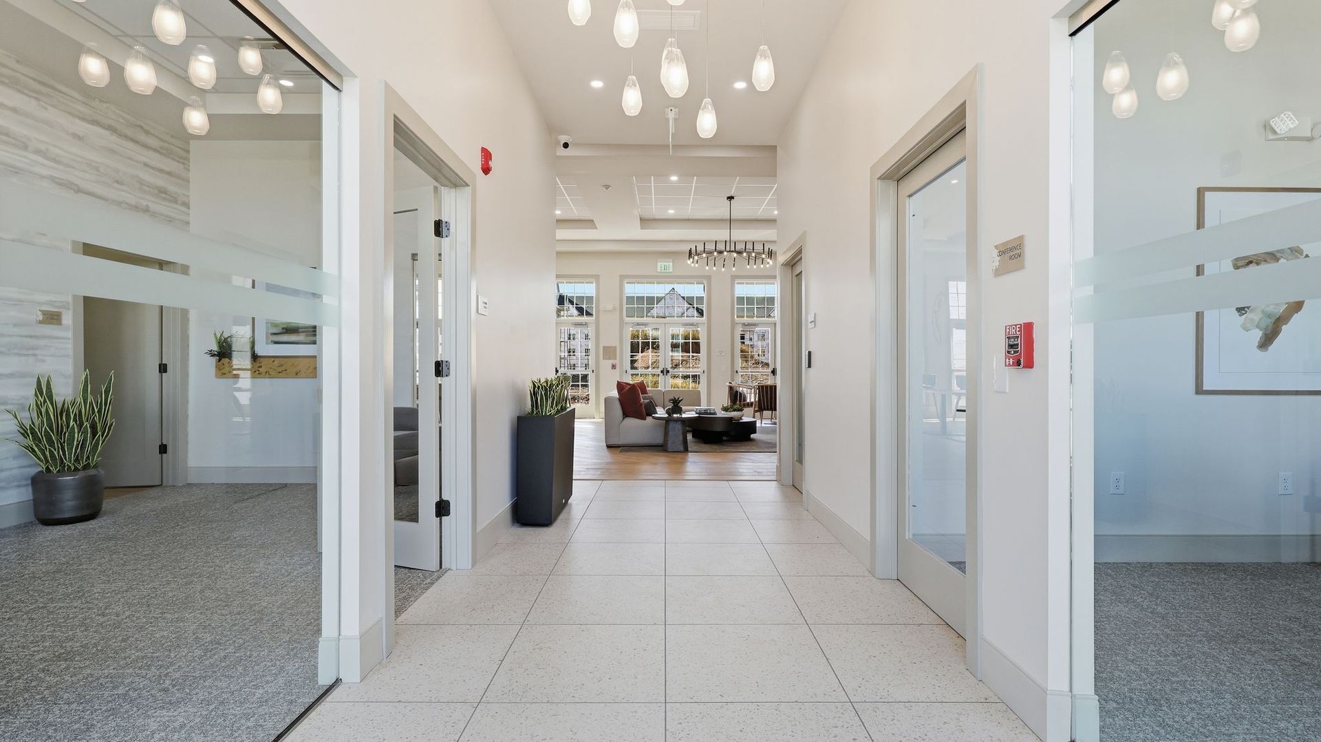 Hallway with white walls, doors, and a tiled floor leading to a furnished lounge area.
