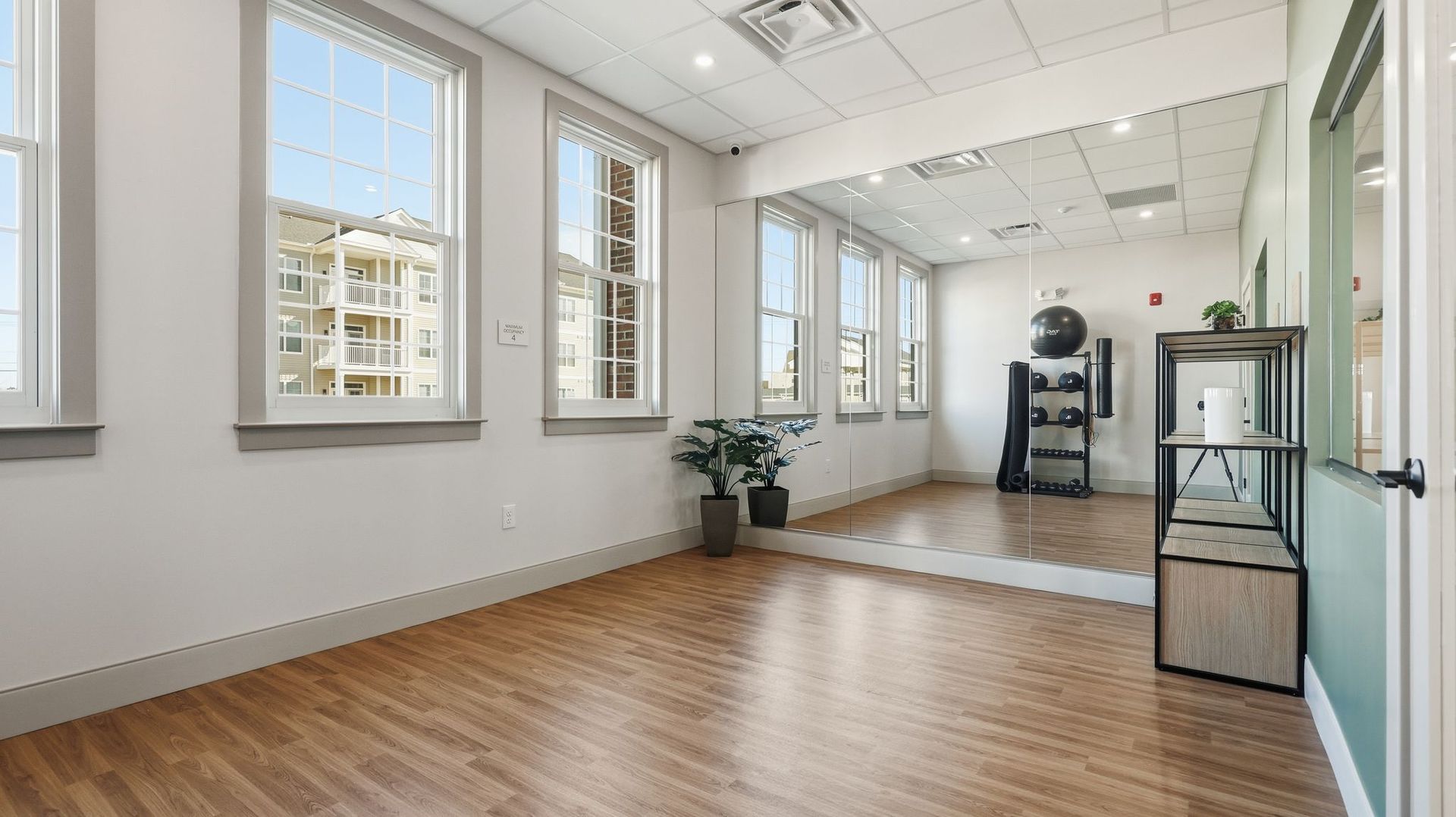 Empty studio with large windows, mirror, and exercise equipment.
