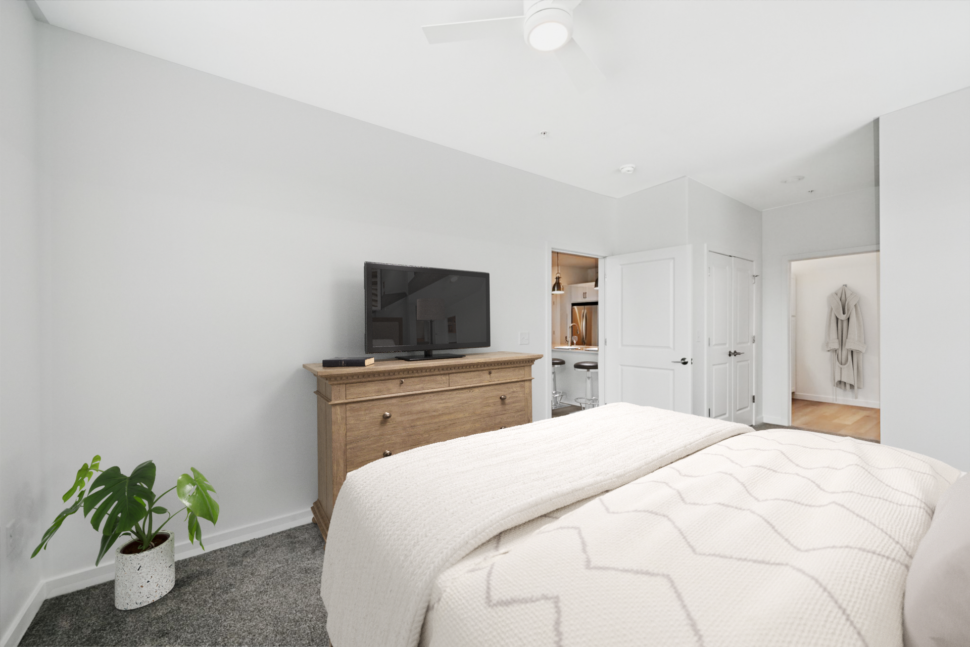 Bedroom with bed, dresser, TV, and Monstera plant against gray walls.