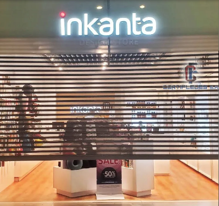 Tienda Inkanta detrás de una persiana metálica parcialmente cerrada, con un letrero luminoso y vitrinas de rebajas