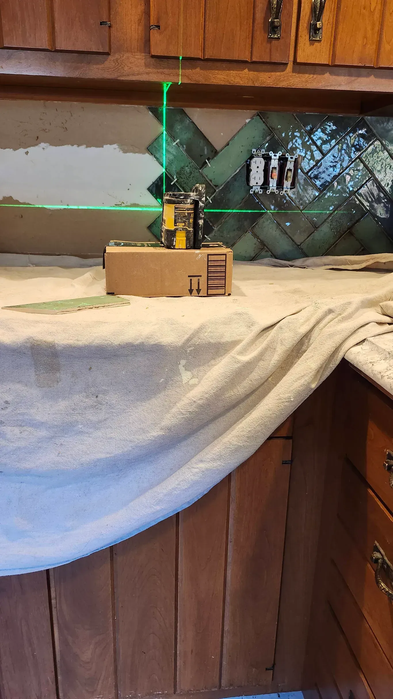 A laser level casts green horizontal and vertical lines across a kitchen backsplash area near electrical outlets.