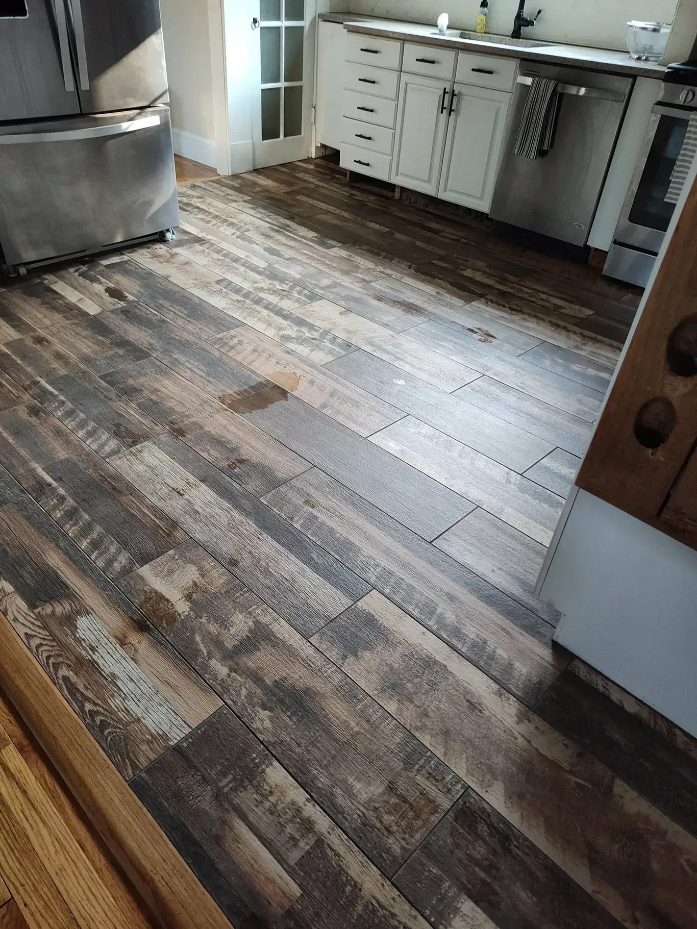 A kitchen with wood-look plank flooring, white cabinets, and stainless steel appliances.