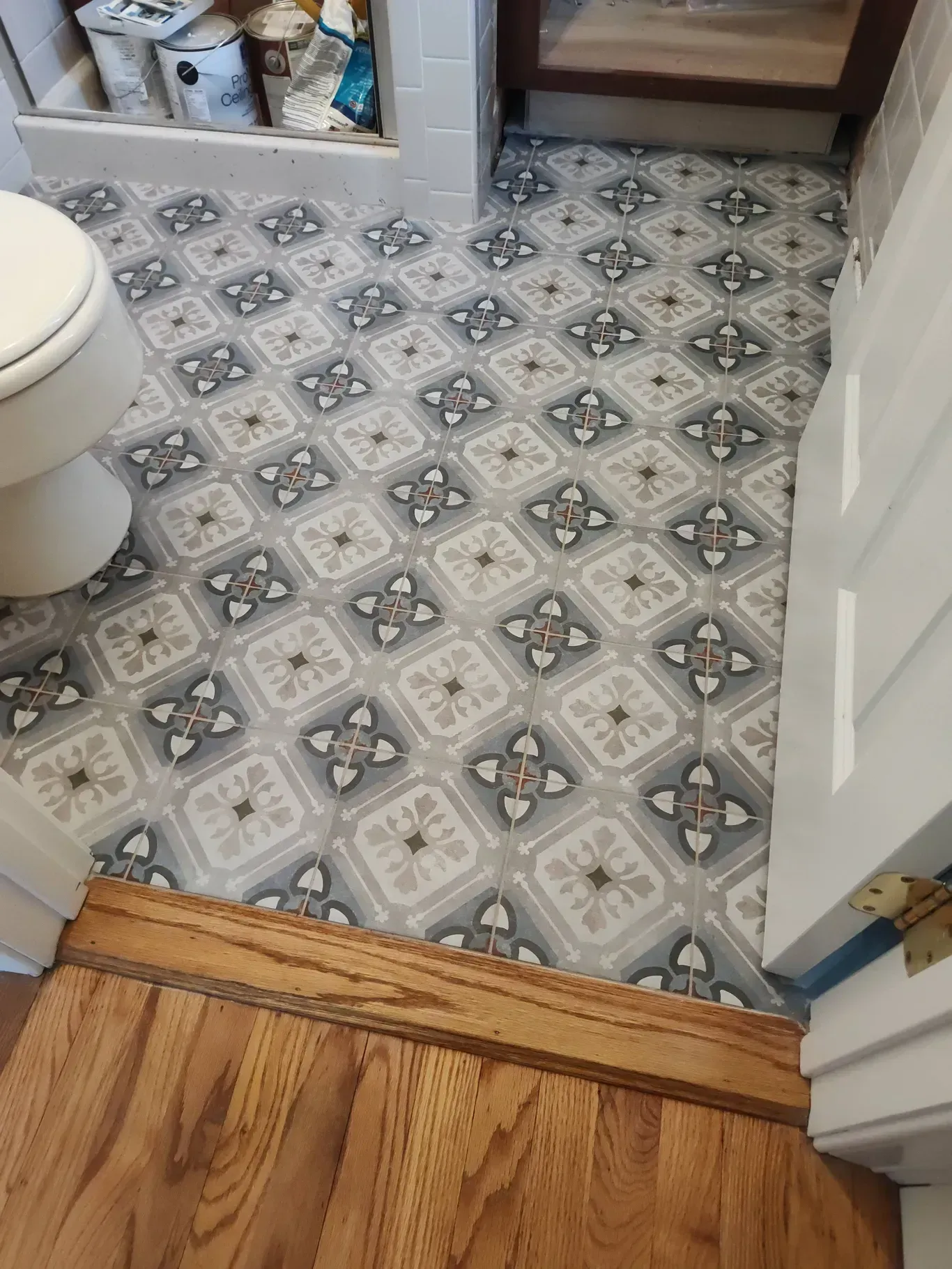 A bathroom floor with grey and white patterned tiles meeting a wooden threshold and doorway.