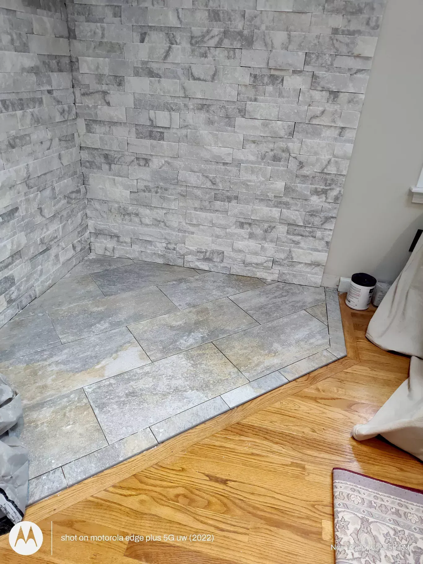 A gray stone fireplace hearth with a textured stacked-stone back wall, bordered by light wood flooring.