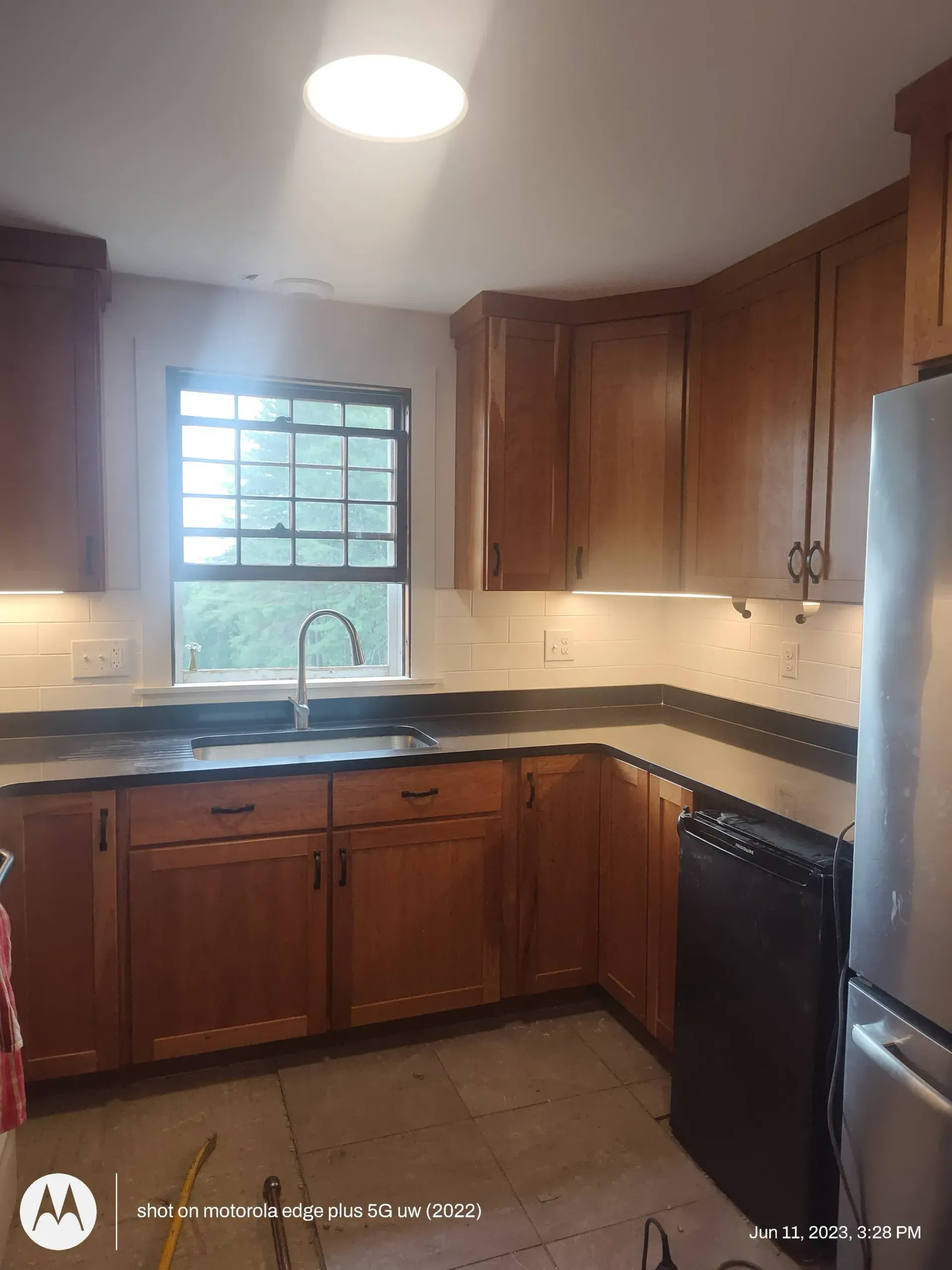 A kitchen with wood cabinets, a dark countertop, a stainless steel sink, and a black dishwasher.