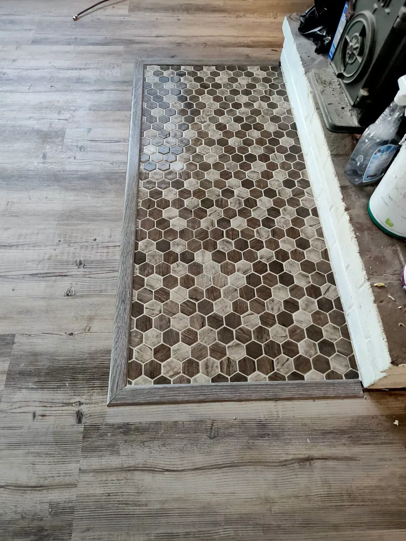 Small hex-tile floor patch beside a gray wood-look floor and white wall trim.