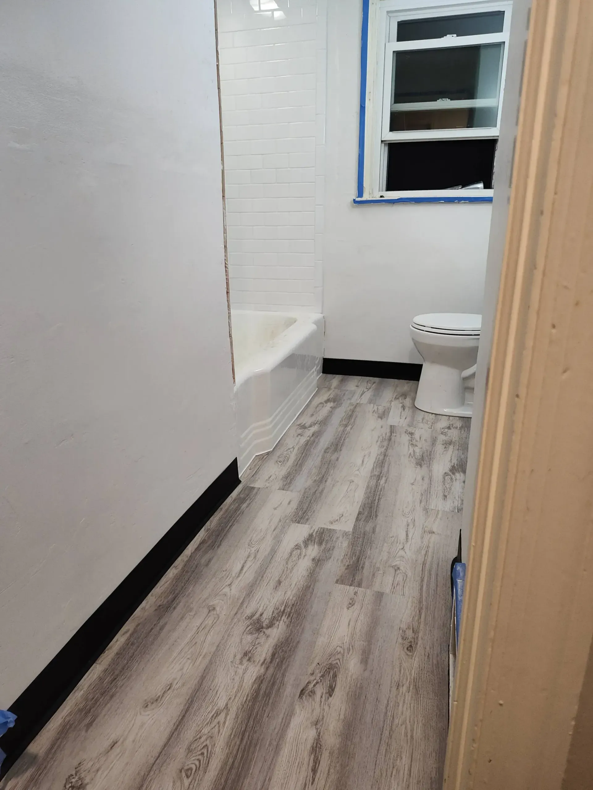A hand installing light-colored wood laminate flooring with a rubber mallet and utility knife nearby.