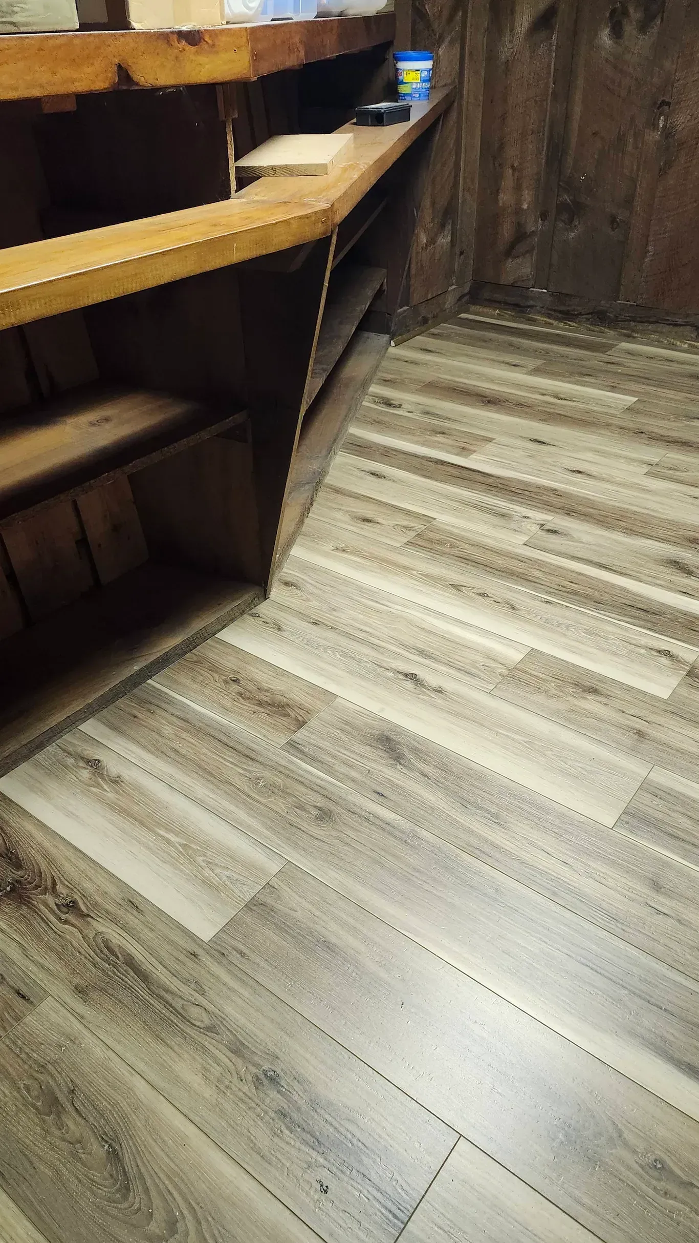 Light-colored wood-look laminate flooring meets a rustic wooden shelving unit in an indoor corner.