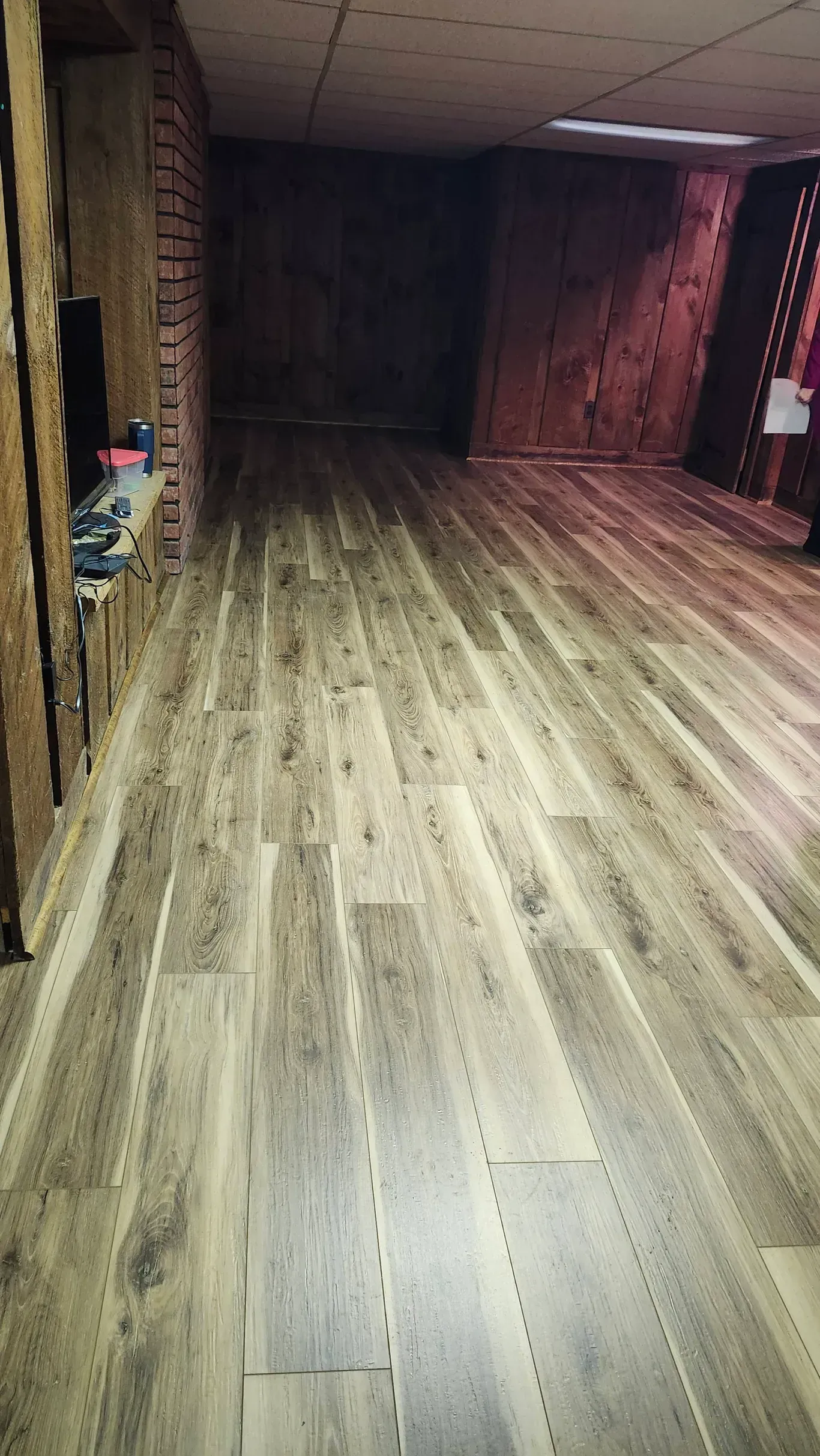 A perspective shot of a room with wood-look laminate flooring and dark, rustic wooden wall paneling.