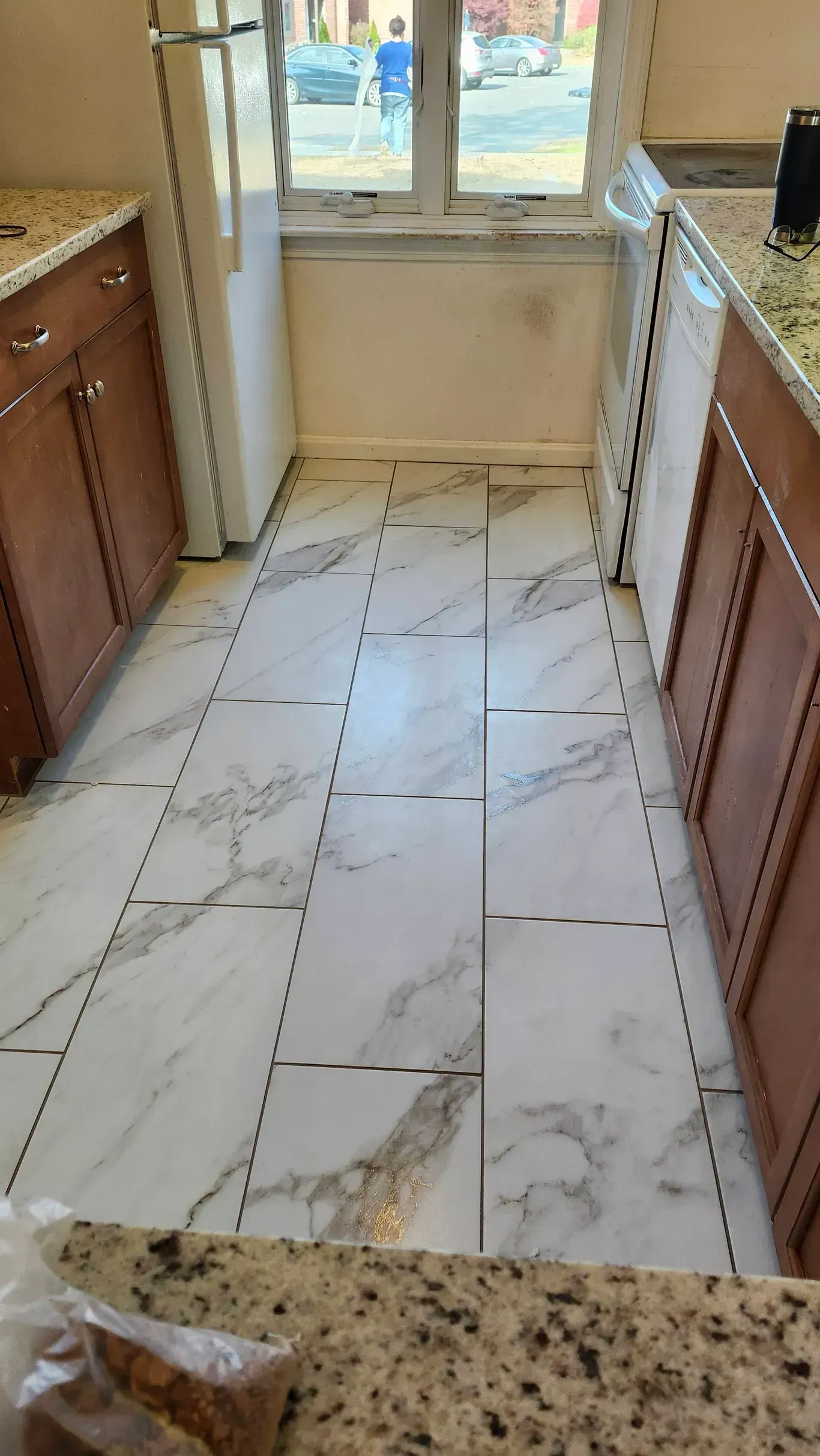 Kitchen floor featuring white faux-marble rectangular tiles installed with visible black grout lines between them.