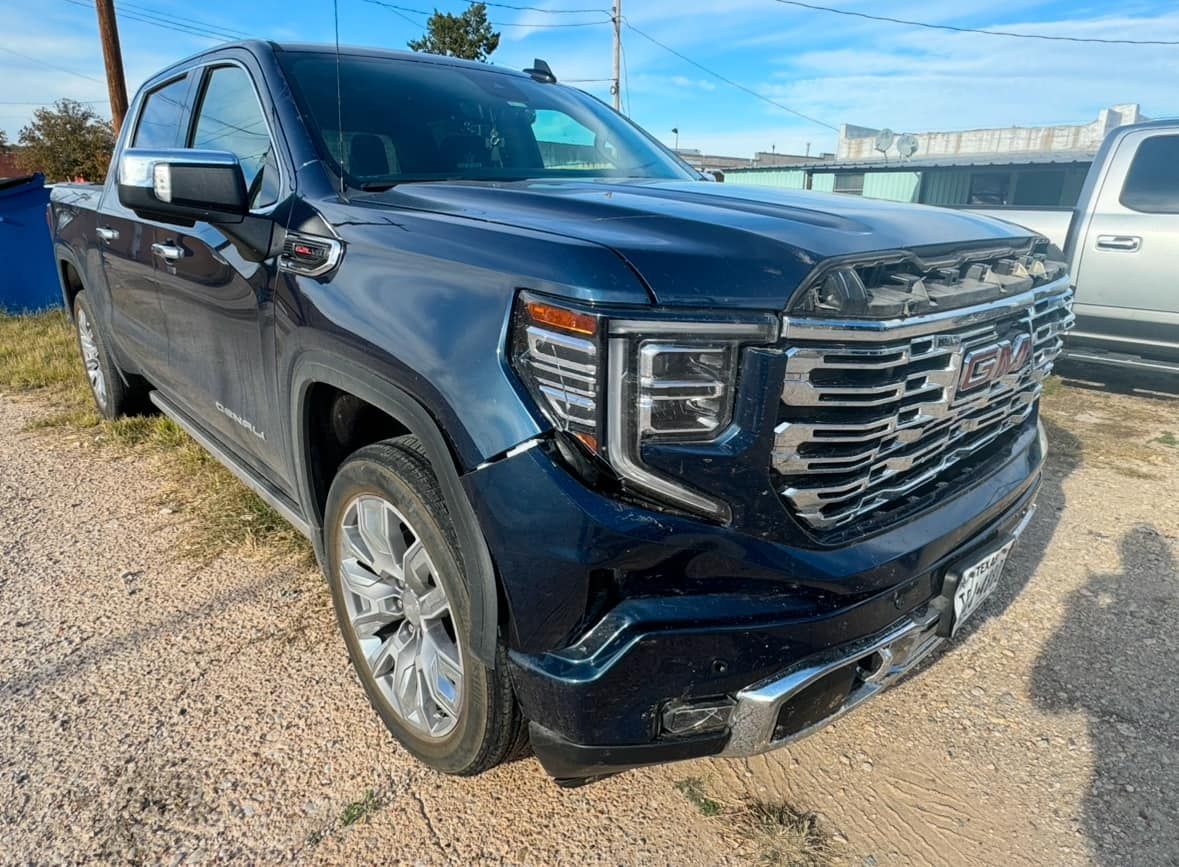 A blue gmc sierra pickup truck is parked in a gravel lot.