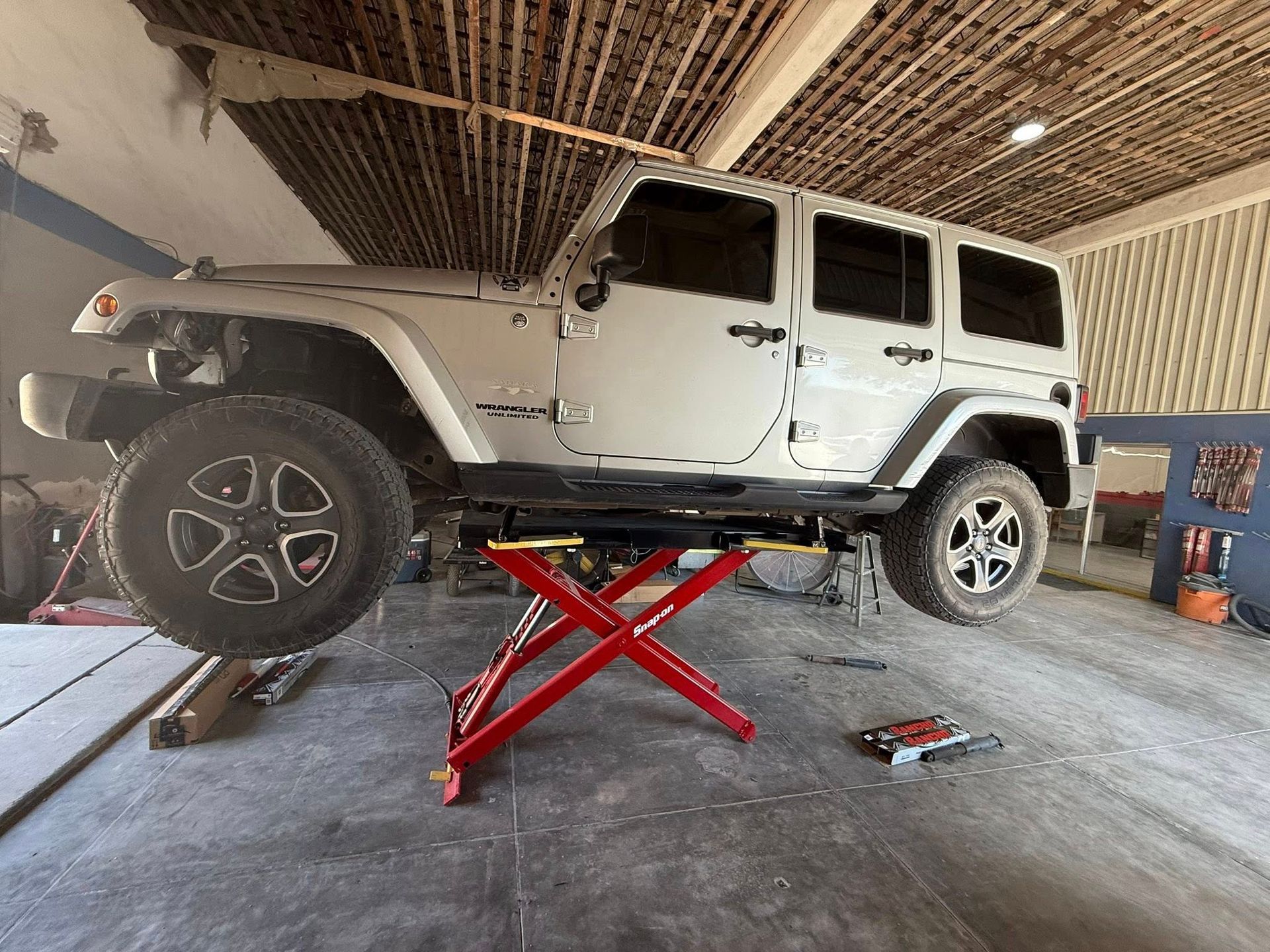 A white jeep is sitting on top of a red lift in a garage.