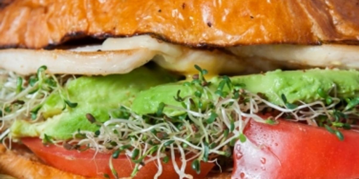 A close up of a sandwich with tomatoes , sprouts and avocado.