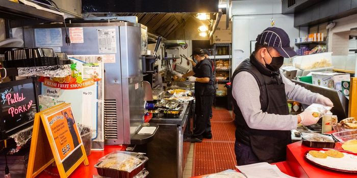 A man wearing a mask is preparing food in a restaurant kitchen.