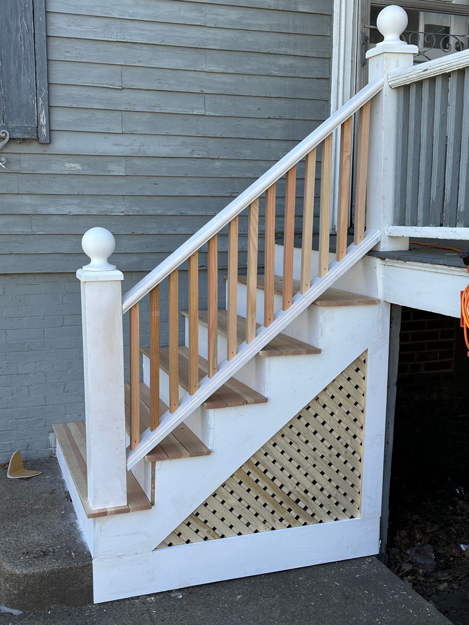 White wooden outdoor staircase with railing and lattice panel beside a house exterior