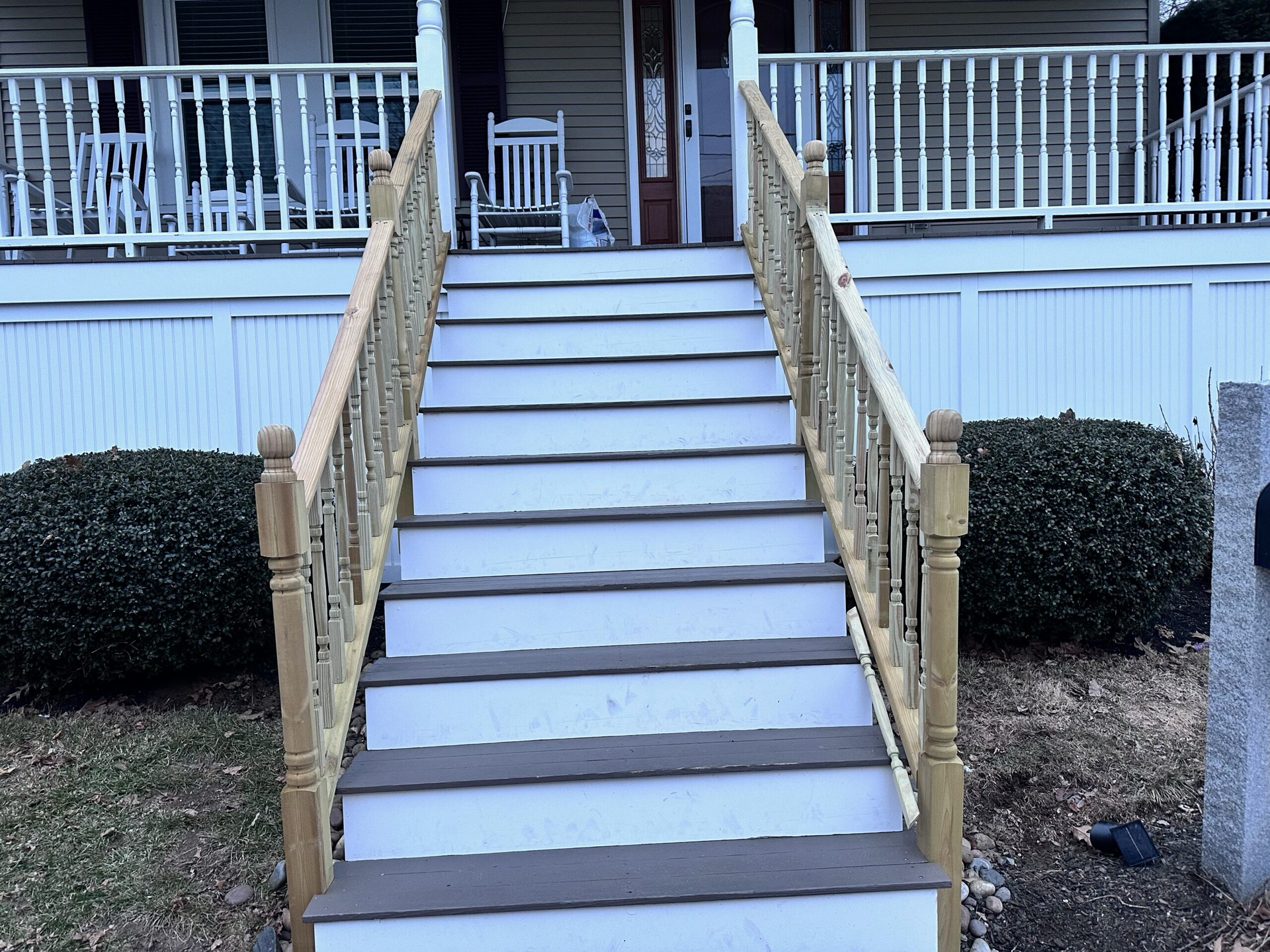 Front porch staircase with tan railings leading up to a white house entrance