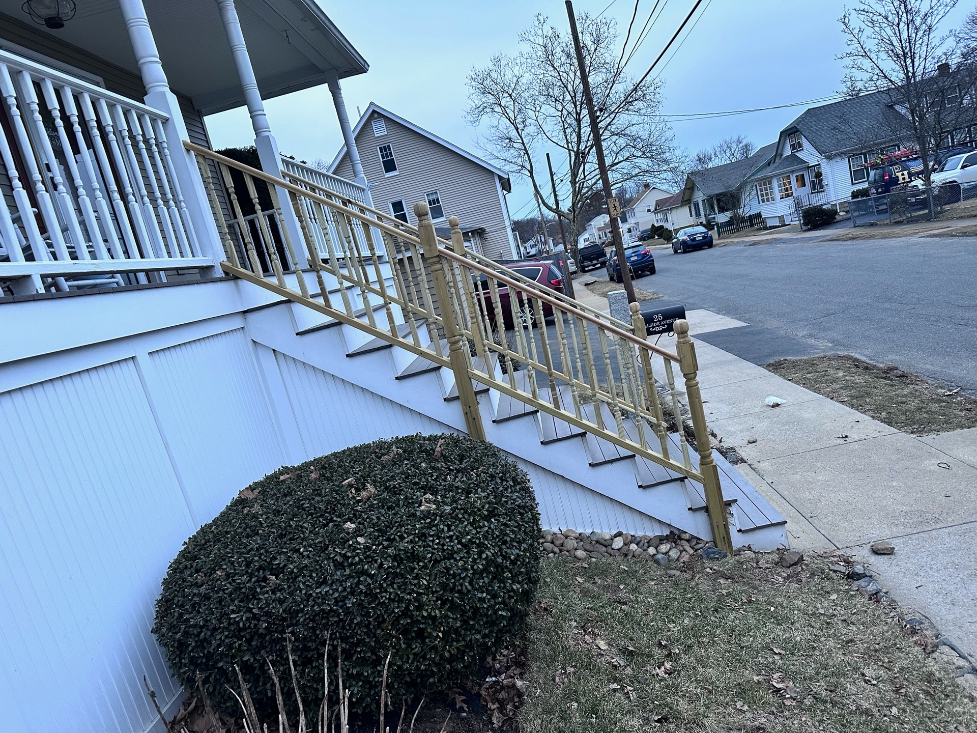Front steps with yellow railing beside a white house on a suburban street