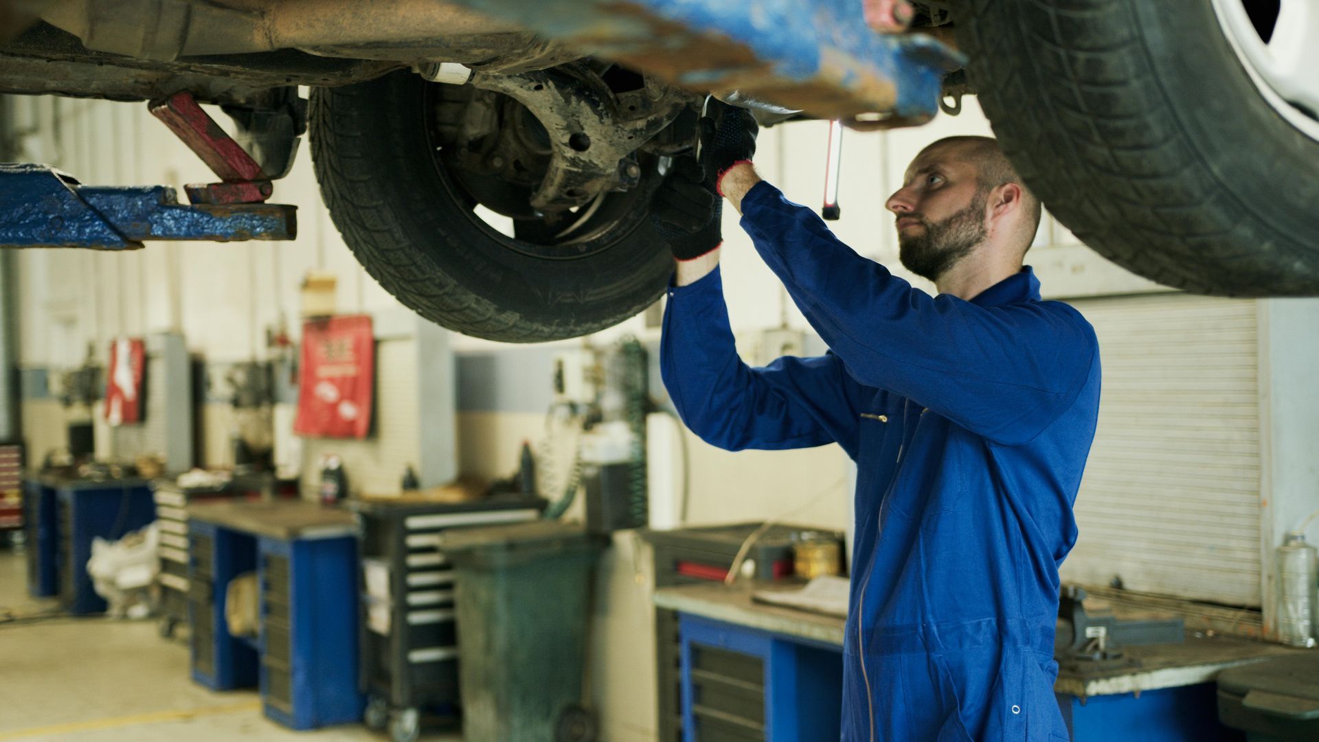 A man is working on the underside of a car in a garage.