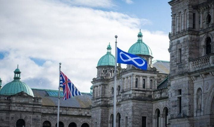 Two flags are flying in front of a large building.