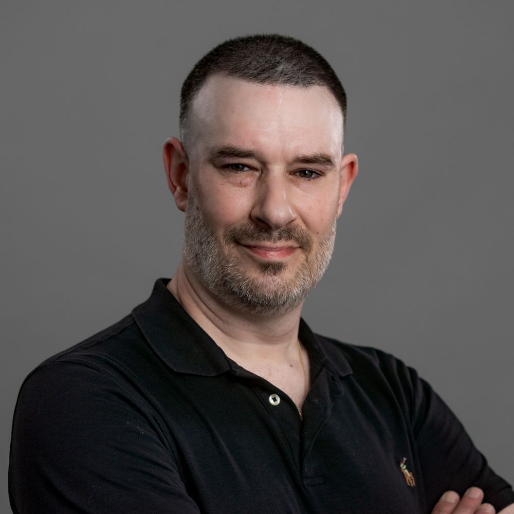 A man with a beard is wearing a black shirt and smiling for the camera.