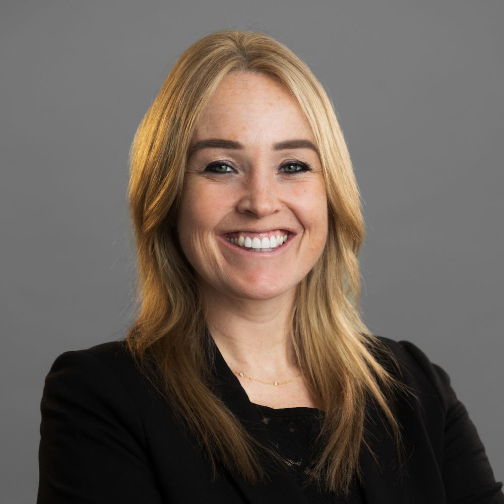 A woman with blonde hair is wearing a black shirt and a blue jacket.