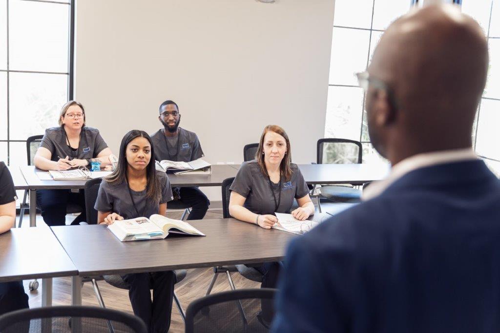 A professor lectures to a class of students in a modern classroom.