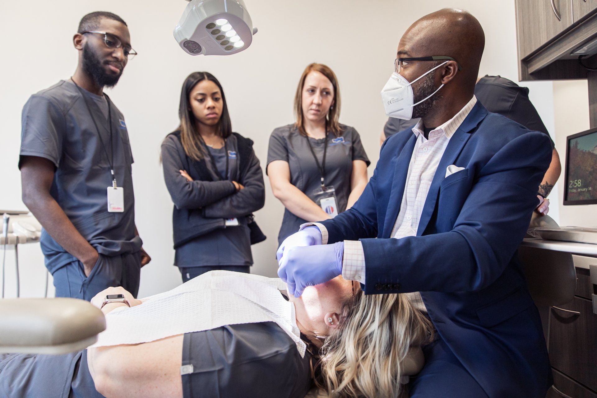 Dentist demonstrating procedure on patient while colleagues observe in a dental clinic.