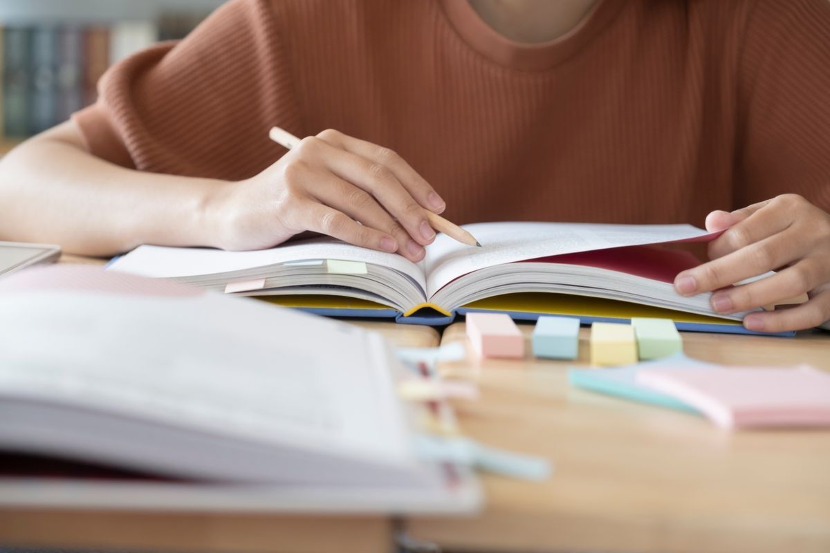 Person writing in an open notebook at a desk with textbooks and stationery.