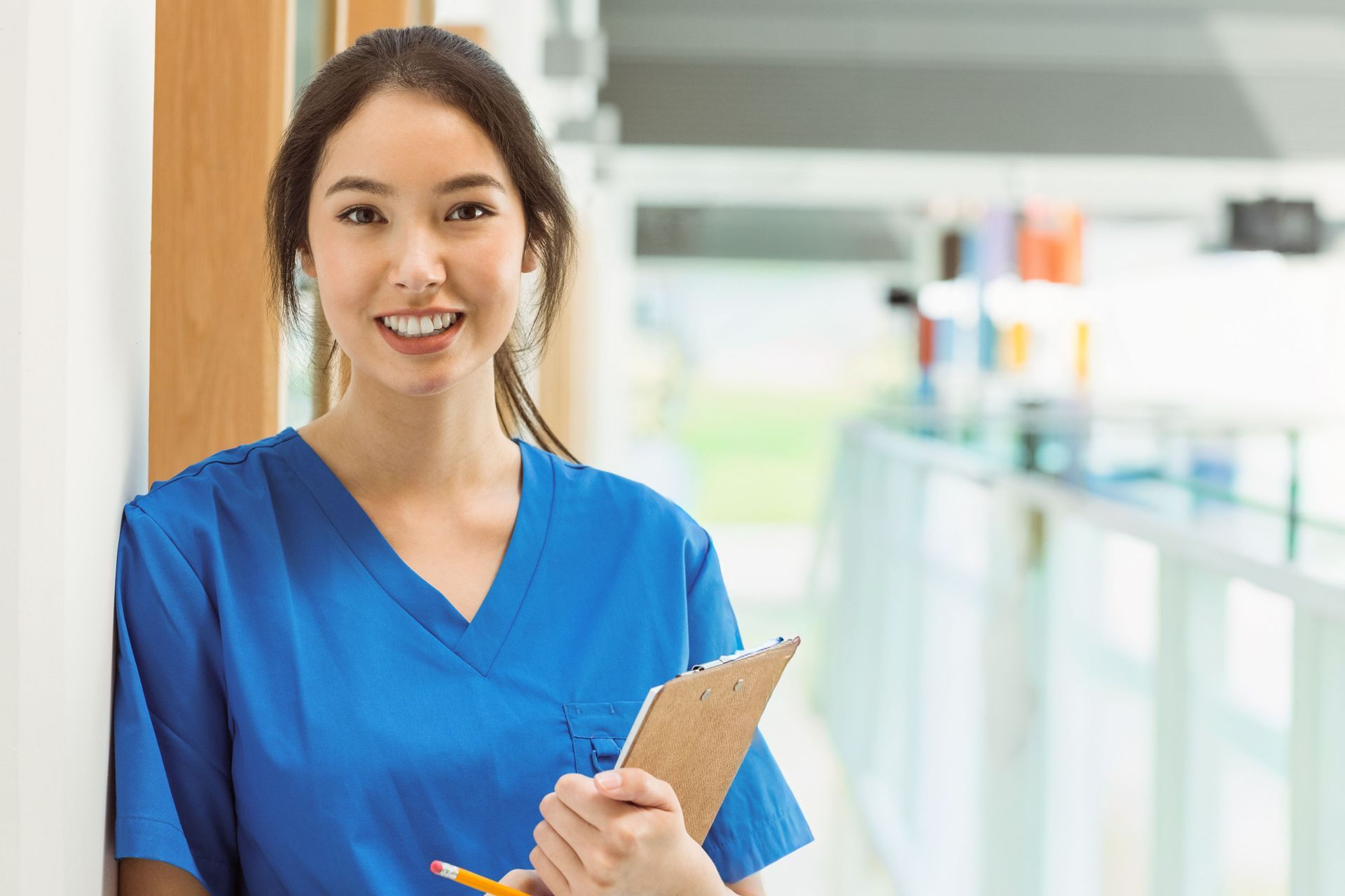Smiling dental assistant in blue scrubs holding a clipboard