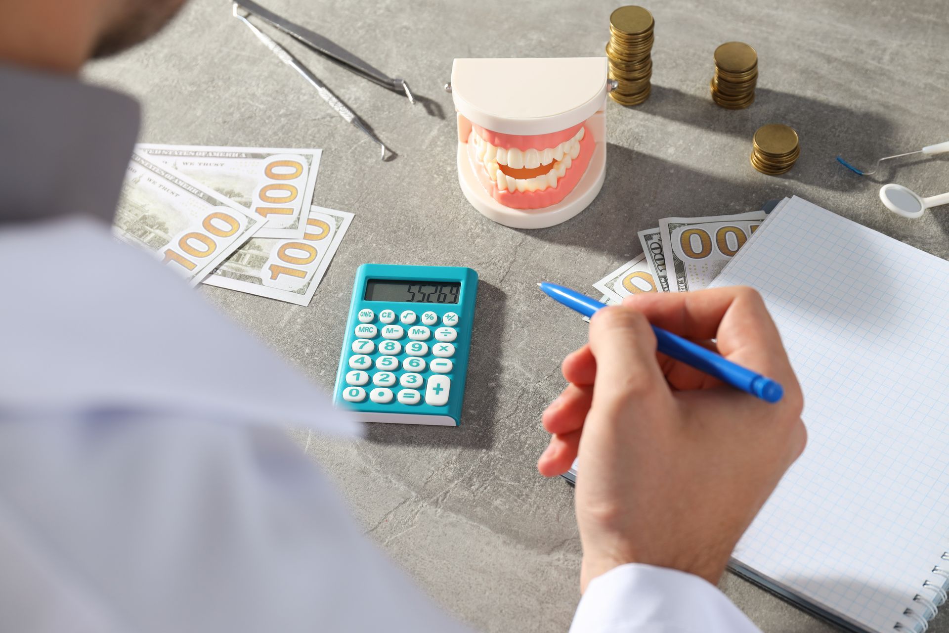Person writing on paper with calculator, money, and coins on a desk