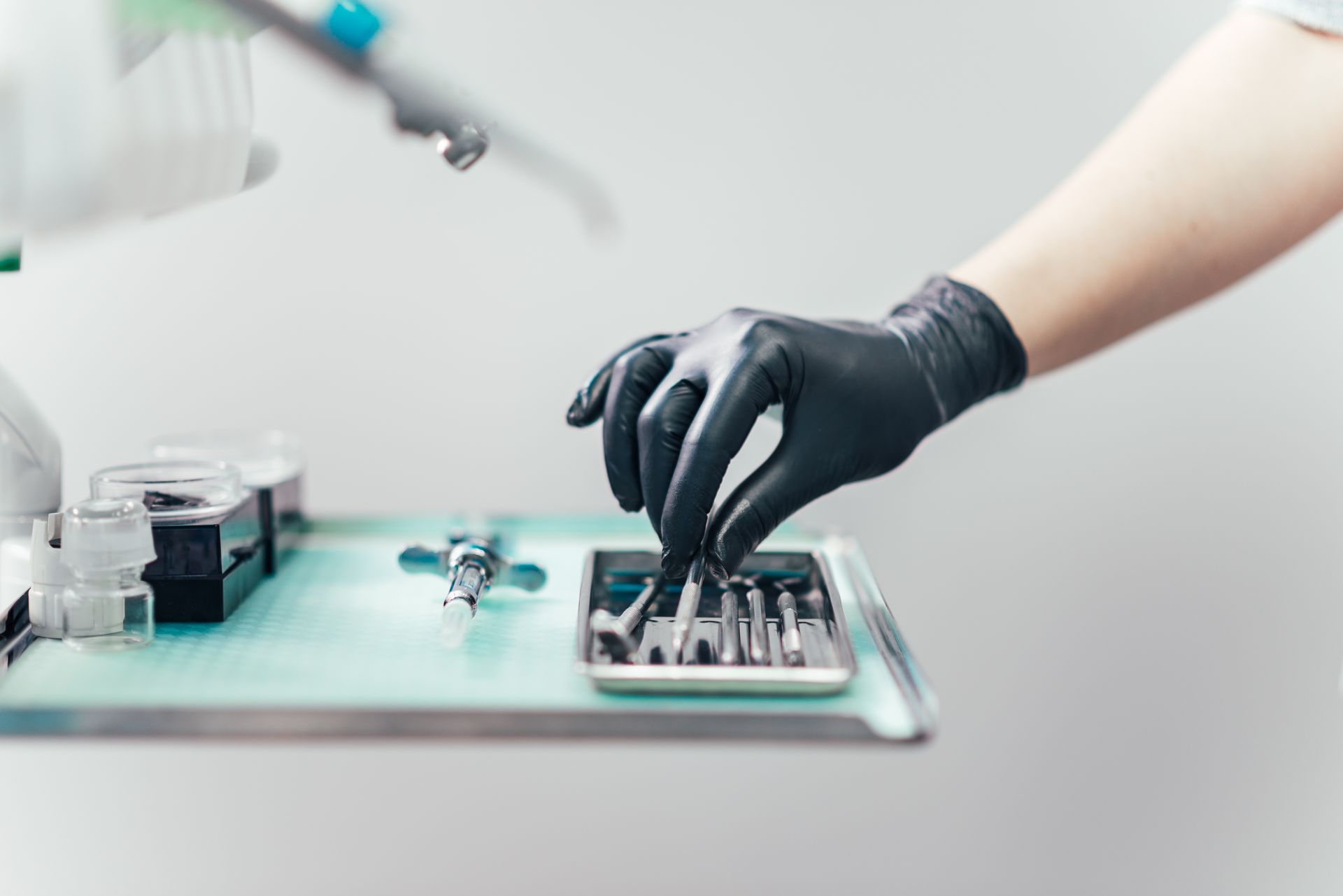 Gloved hand handling dental tools on a tray in a bright clinic setting