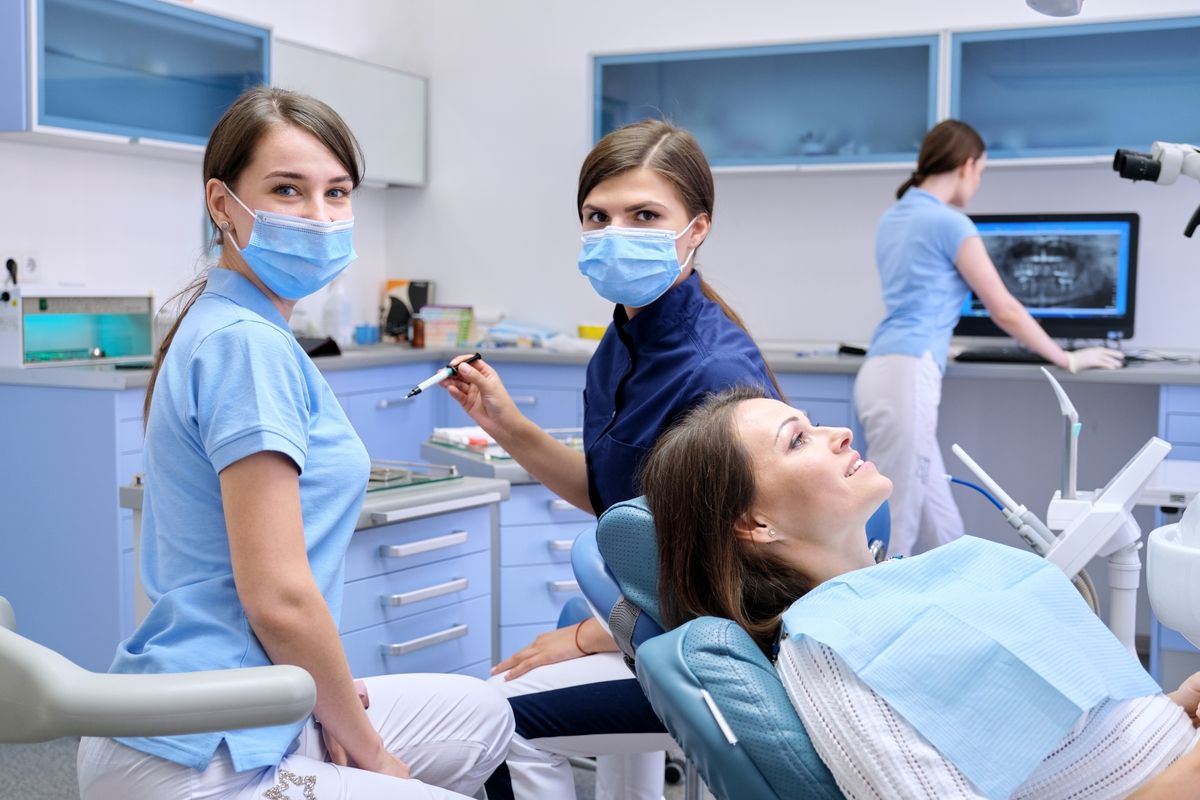 Dental clinic with masked staff treating a reclining patient in a bright, modern exam room