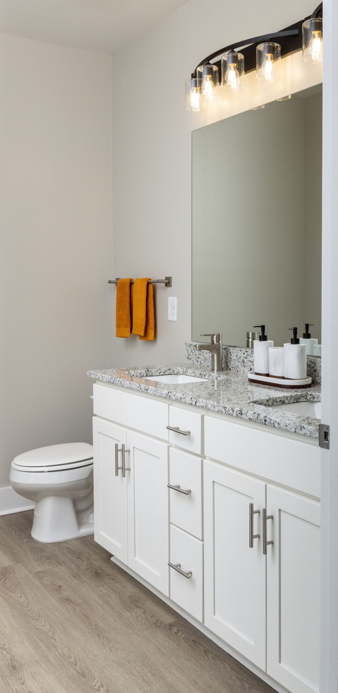 Bathroom with white cabinets, speckled countertop, large mirror, and orange towels.