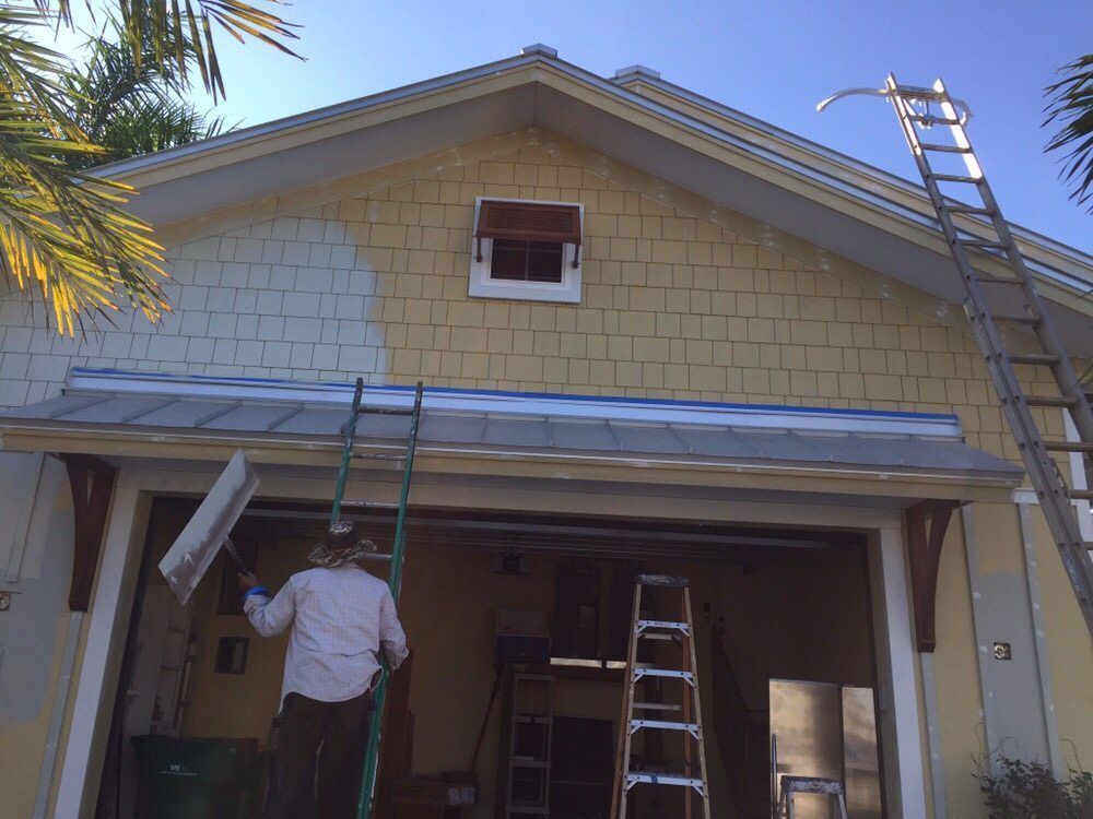 A man is standing on a ladder painting the side of a house