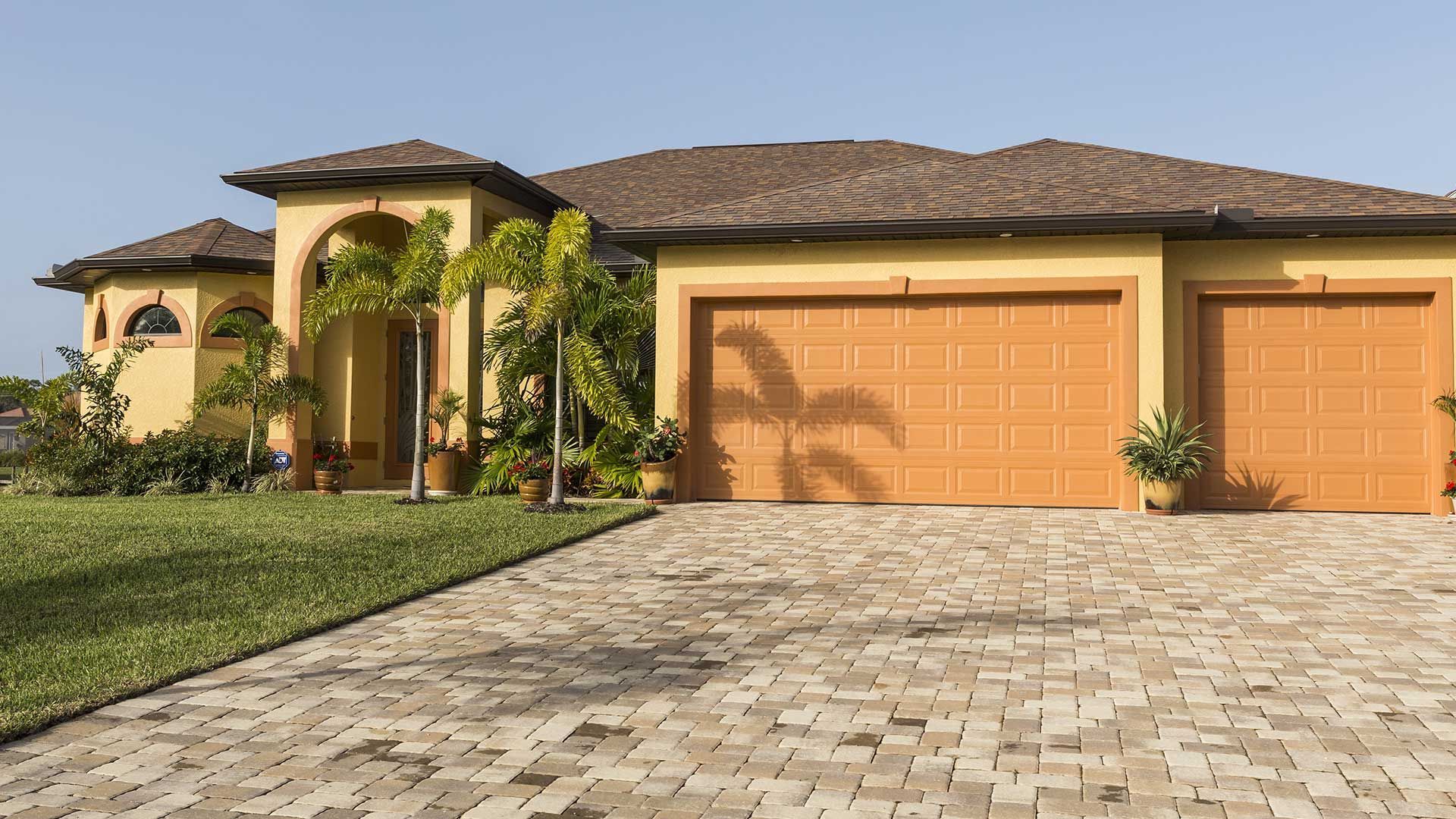 A large house with two garage doors and a brick driveway.