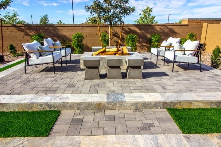Modern patio with gray paver flooring, outdoor chairs, and a central stone fire pit surrounded by concrete stools.