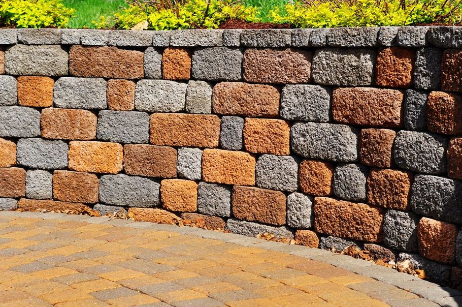 A curved retaining wall built from multi-colored, textured stone blocks, bordering a paved patio area.