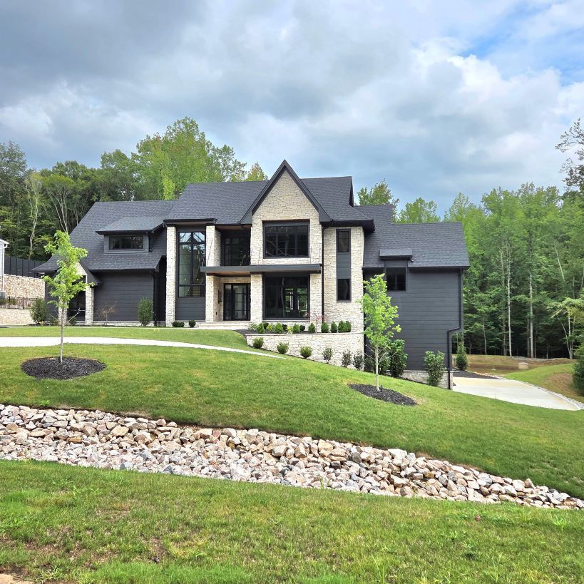 Modern two-story stone-and-gray house with a landscaped lawn and driveway under a cloudy sky
