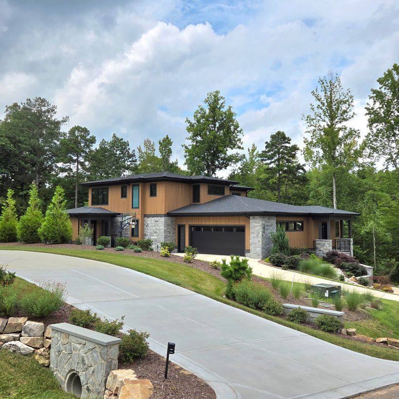 Modern two-story house with a curved driveway, stone accents, and landscaped yard under a cloudy sky