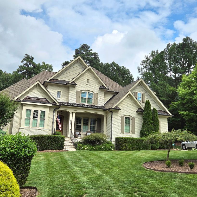 Large beige suburban house with a manicured green lawn and driveway under a partly cloudy sky