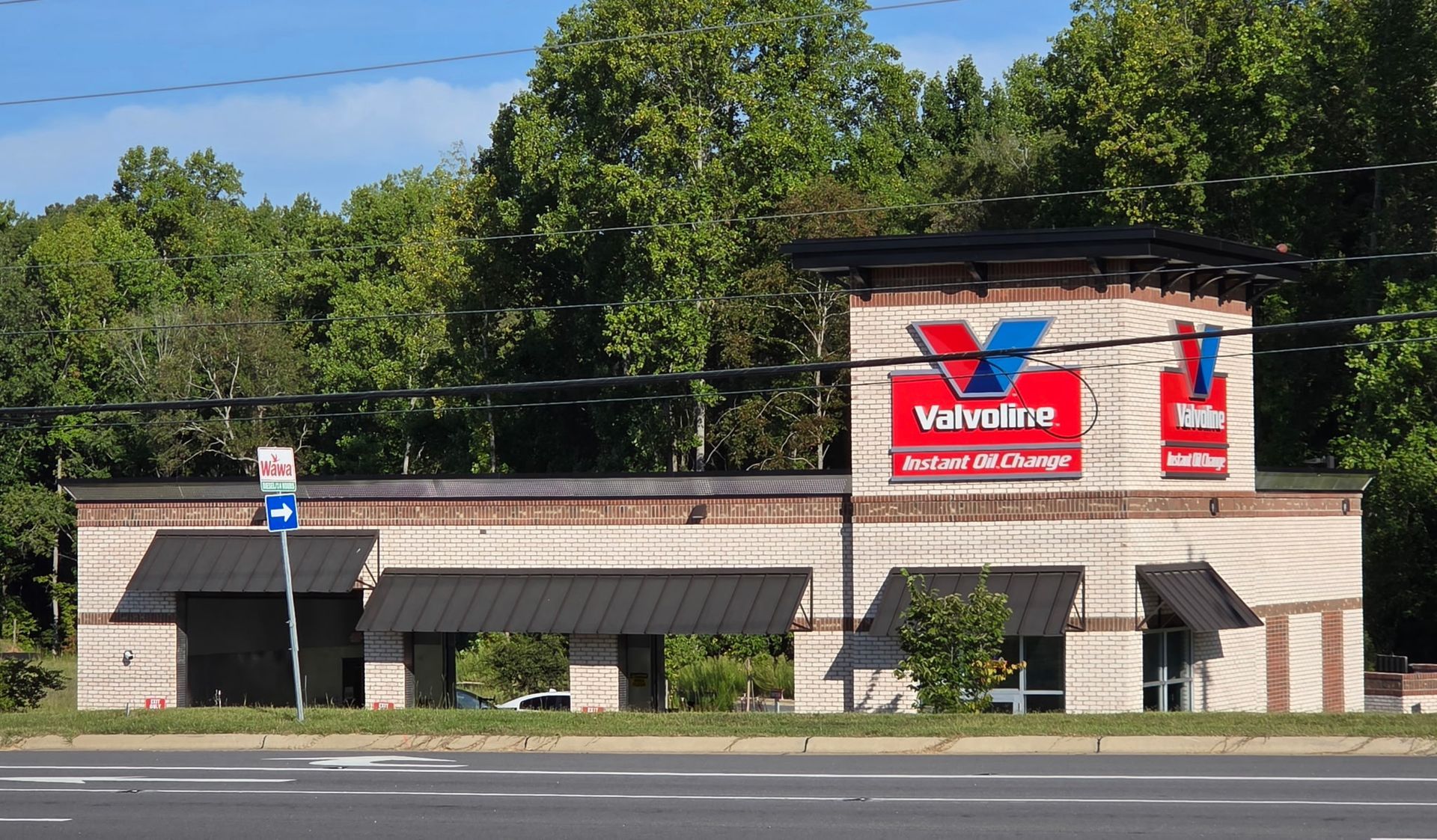 Valvoline oil change shop with beige facade and red signage along a roadside, trees behind it